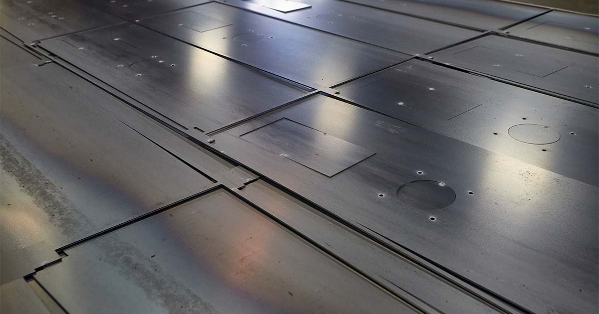 Smoothly finished metal sheets with various shapes and cutouts, arranged after laser cutting.